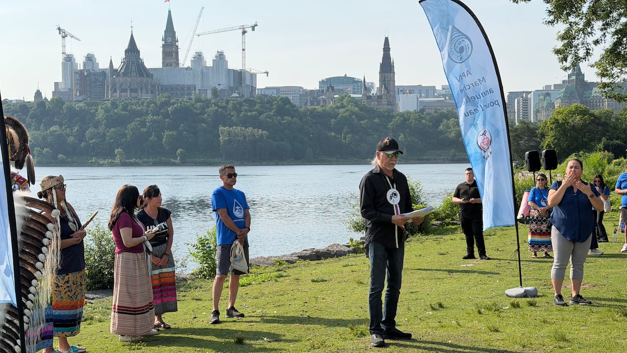 A man gives a speech with the Ottawa River behind him and Parliament Hill looming on the other side.