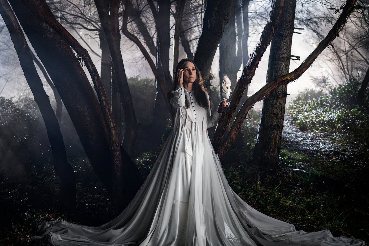 Woman in long white dress stands in the middle of the forest.
