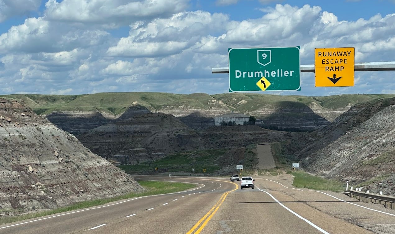 a highway going down a hill, a road sign that says Drumheller