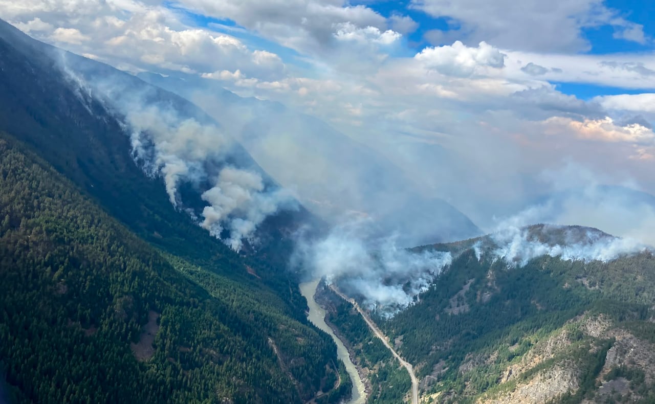 Wildfire smoke rises out of a valley with a river running through it.