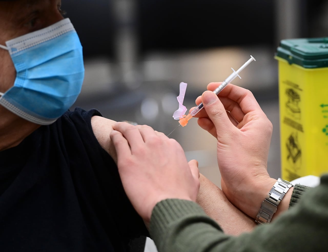 A patient wearing a mask gets a vaccine injected into their upper arm.