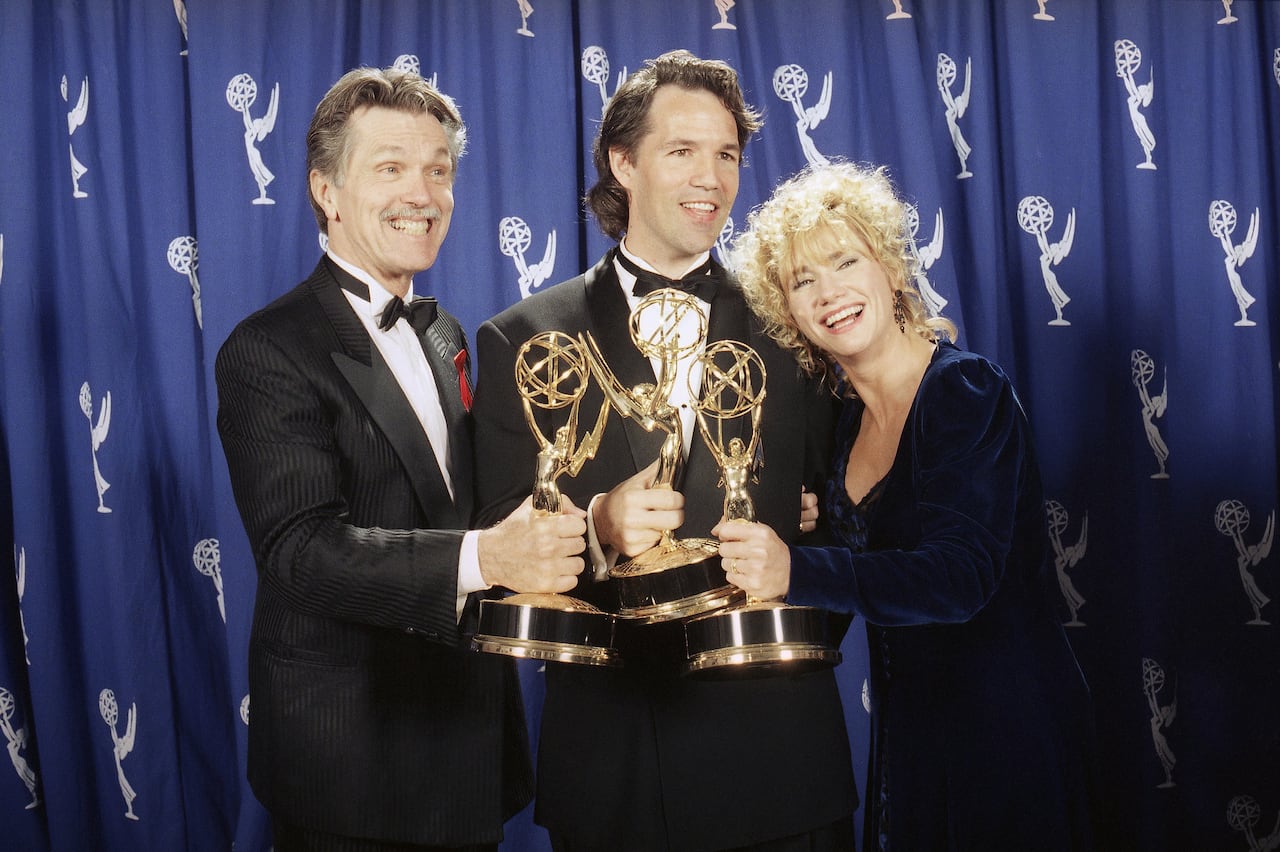 Two men and a woman hold Emmy awards.
