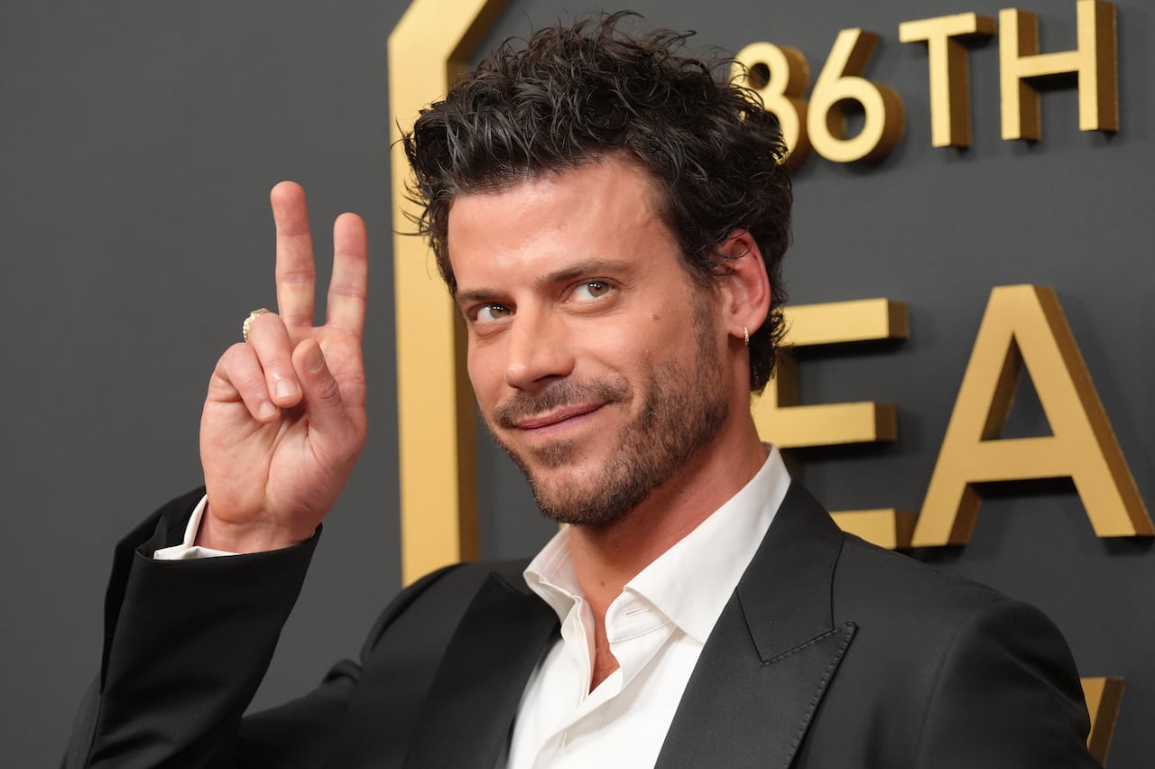 A man in a dark grey suit smiles and flashes a peace sign