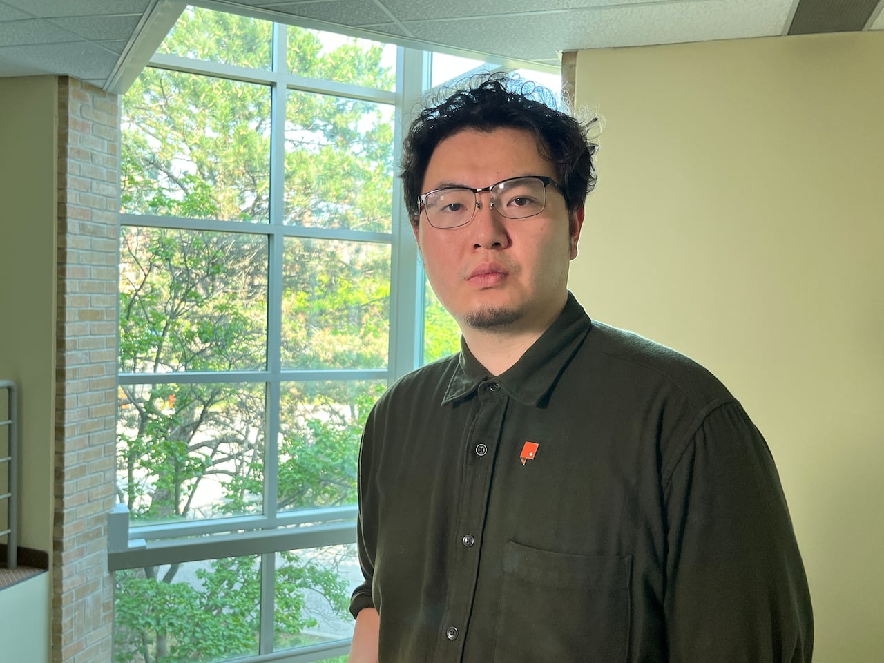 An Asian man in a green button up shirt with dark hair.