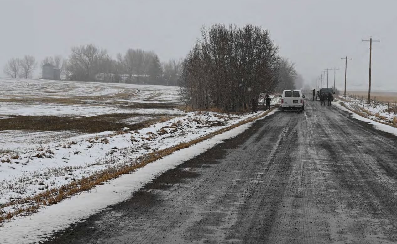 A rural highway with a police car parked near some trees on a grey, wintery day.