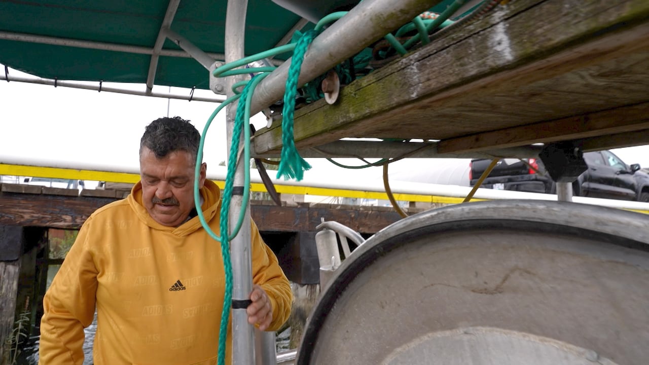 A fisher on a boat, turning a net wheel.