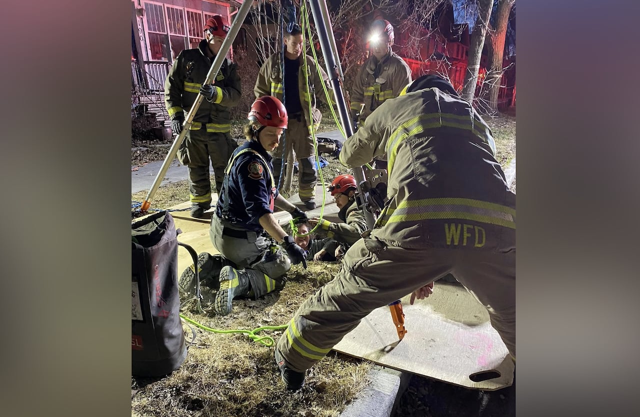 Firefighters work to help a woman out of a sinkhole on a grassy boulevard.