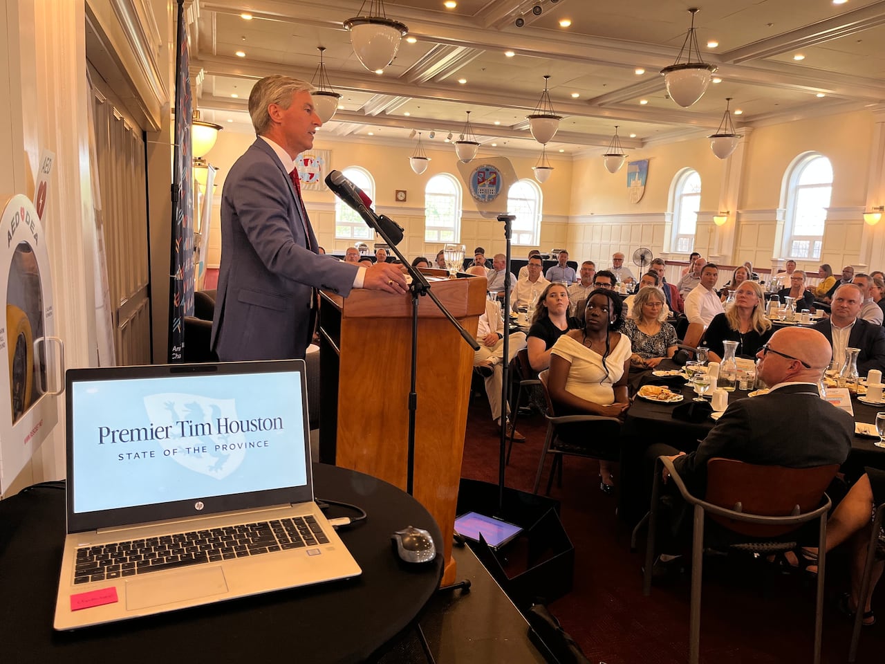 Man at podium speaks to a room full of people seated at tables.