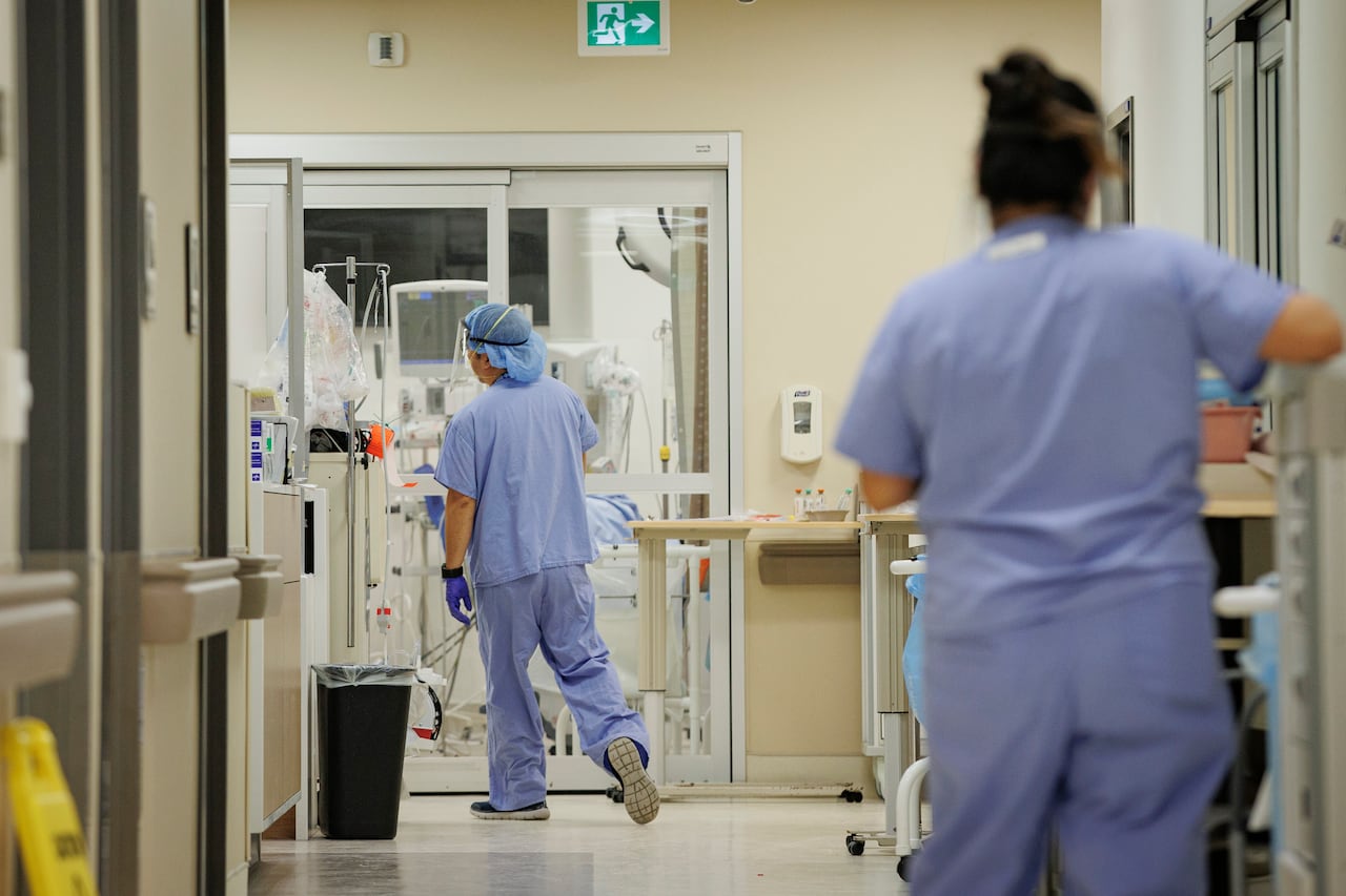 Two nurses, one in the foreground on the right but out of focus, and one walking on the left.