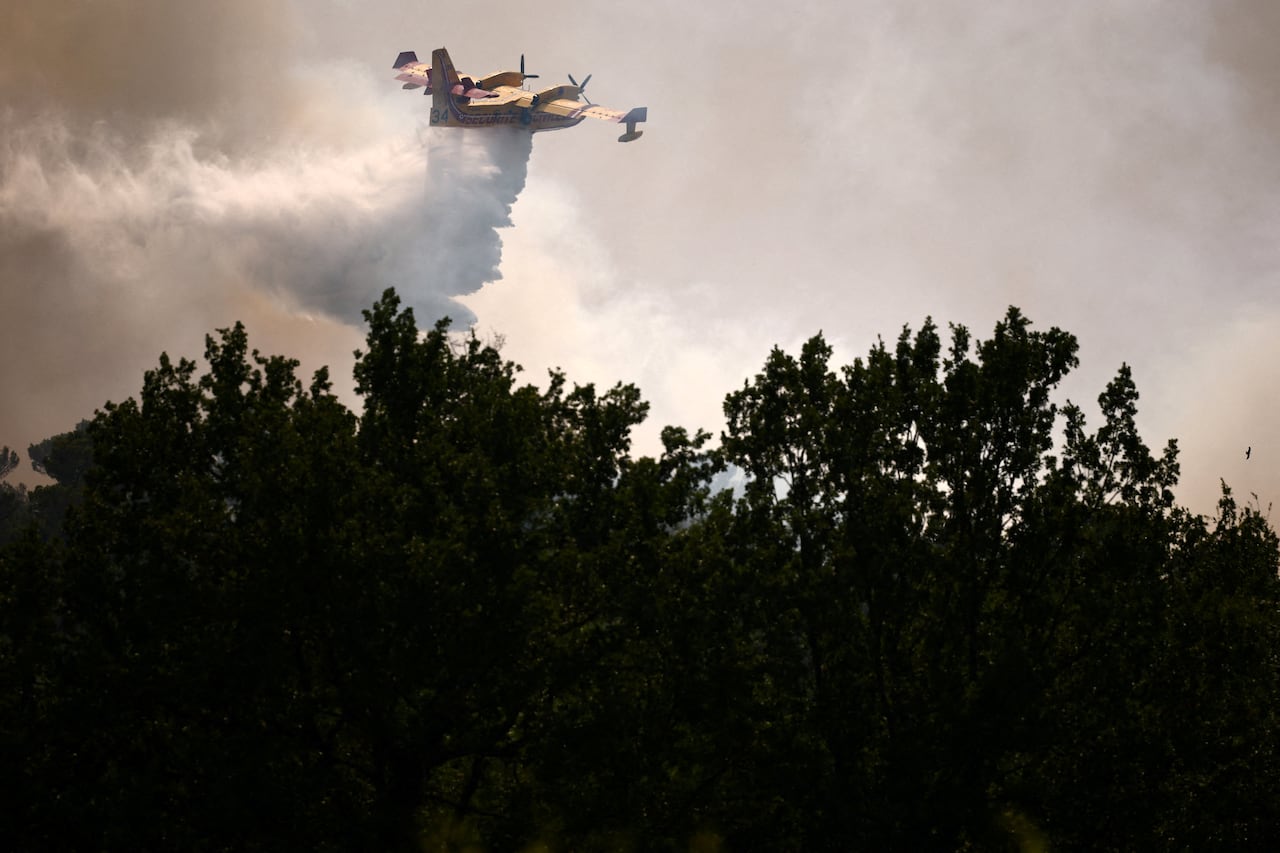 A yellow plane dumps water over a forest in a smoky sky.