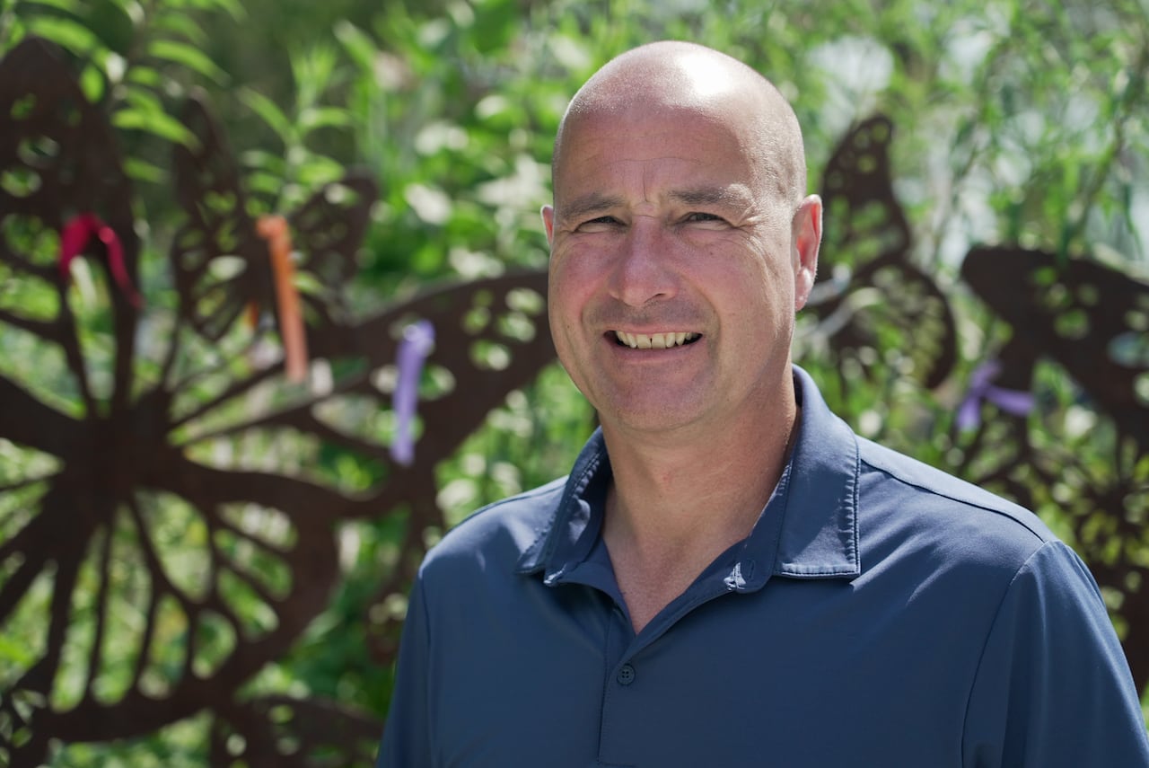 A close-up of a person in a garden, smiling.