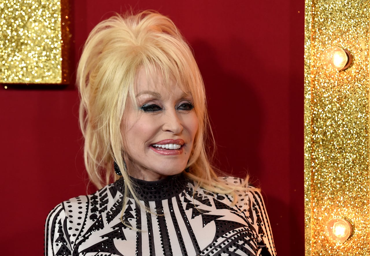 A blonde woman in a black-and-white pattered shirt in front of a red and gold backdrop.