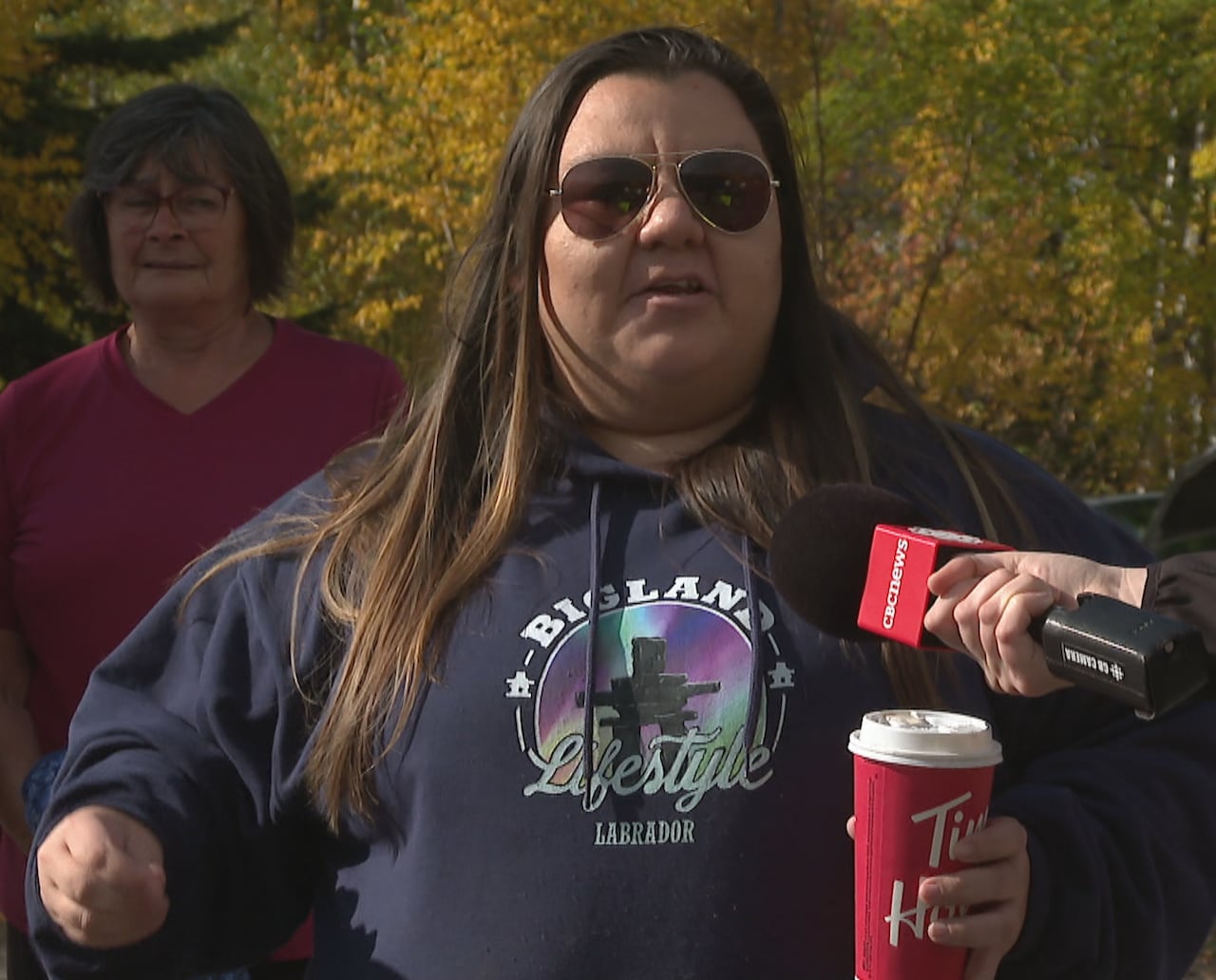 A woman in sunglasses and a dark sweatshirt gestures with her hands.