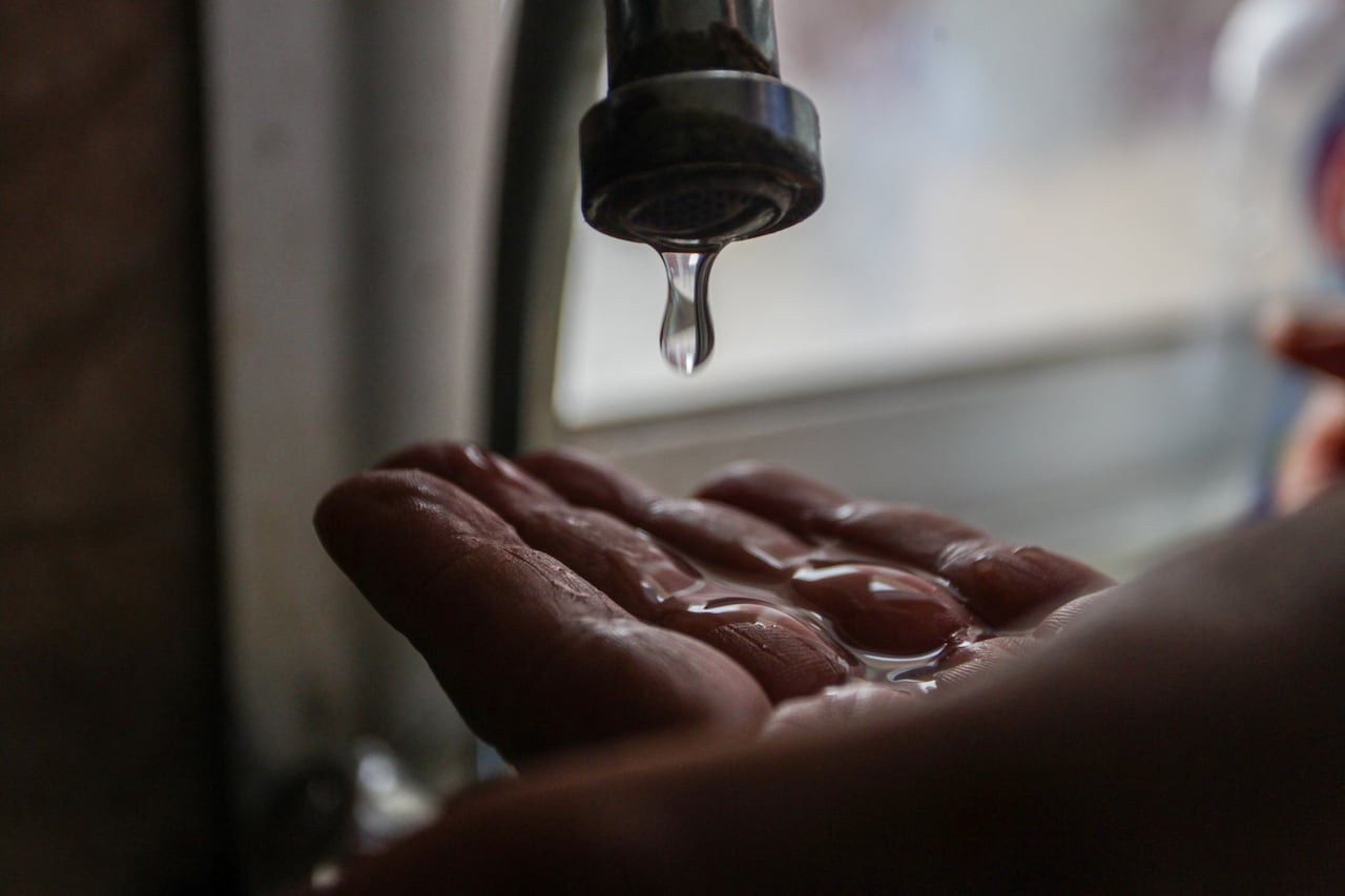 A hand is placed under a faucet with water droplets slowly falling.