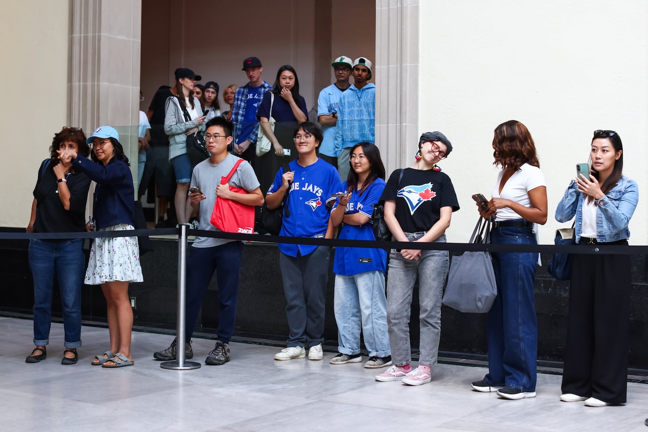 Eight people stand side-by-side behind a black line with Blue Jays merch.