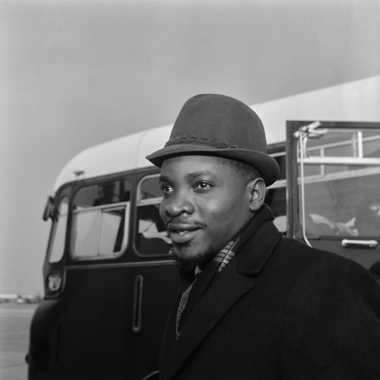 A black and white photograph depicts a dark complected man wearing a hat outdoors.