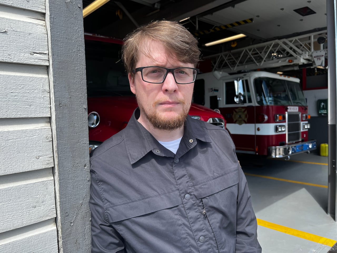 Man leaning against door frame, there's a firetruck behind him.