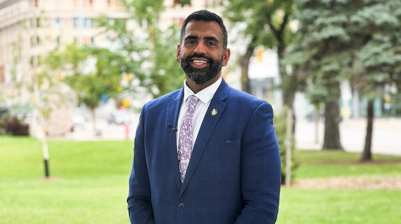 A man in a suit smiles outside.
