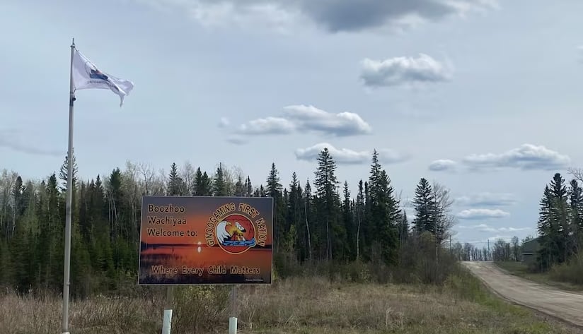A sign next to a road welcomes people to Ginoogaming First Nation