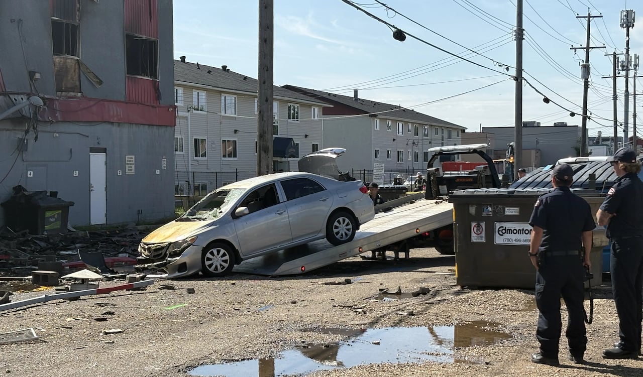 A damaged vehicle is being pulled onto a flatbed tow truck away from a fire-damaged building.