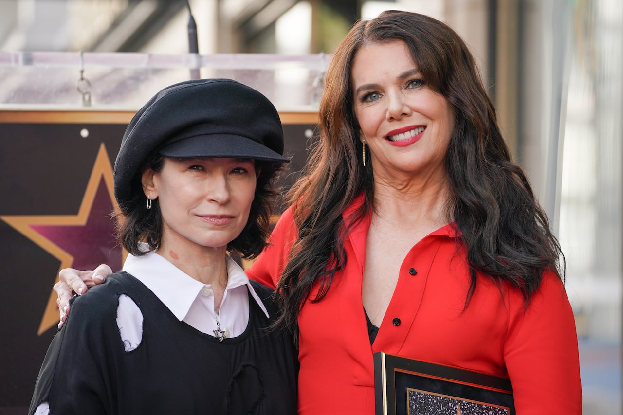 A picture of a woman wearing a red dress posing beside another woman wearing a black sweater and hat.