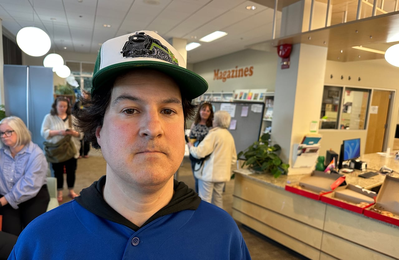 A man wearing a baseball cap stands in a library.