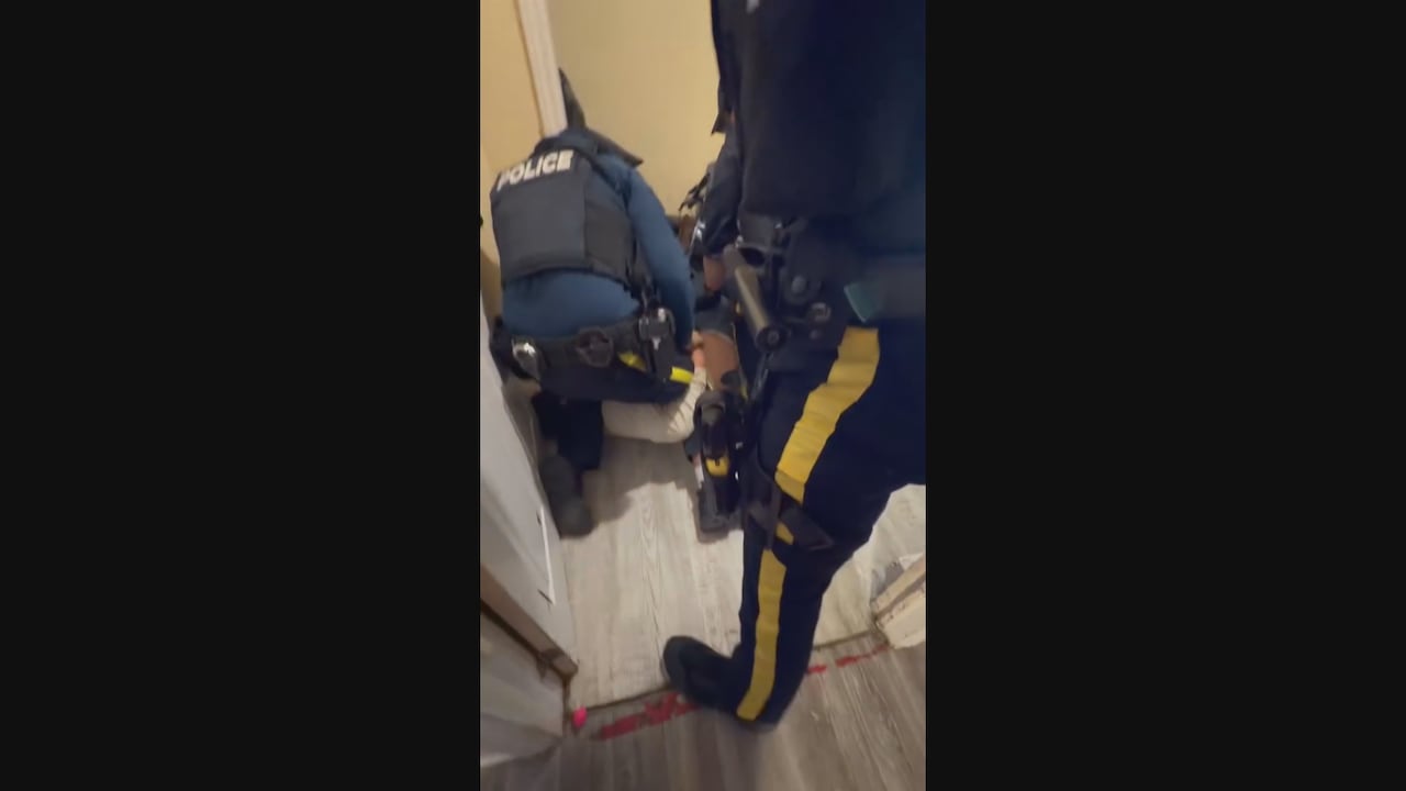 一名男子在地面上，两个警察压制他，一个警察站在门口阻止他人靠近