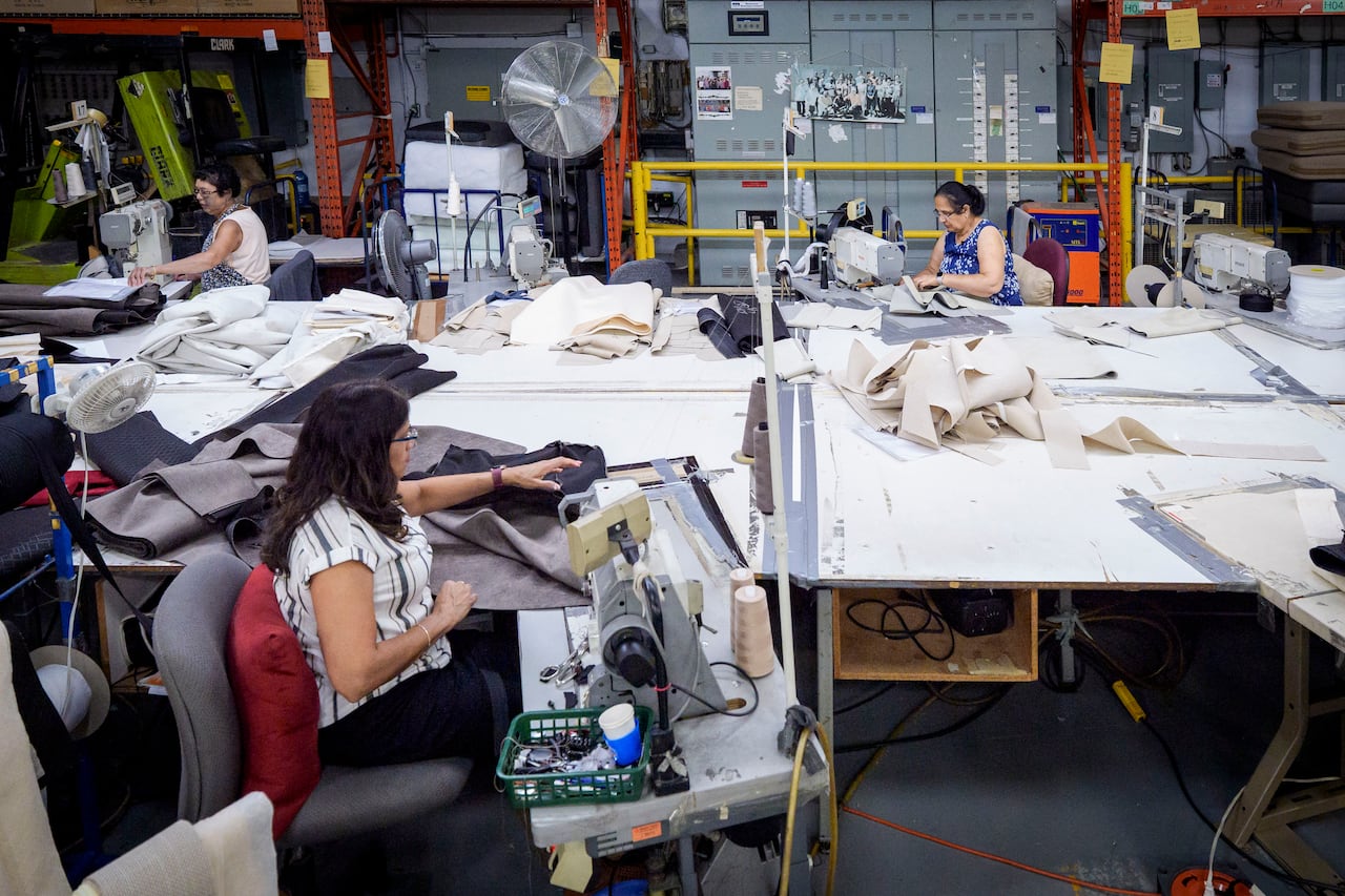 Three woman sitting at industrial sewing machines, working in a furniture factory.