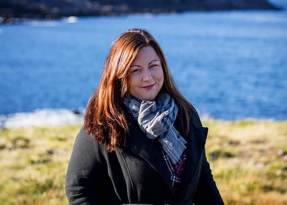A woman smiling at the camera, standing in front of the ocean.