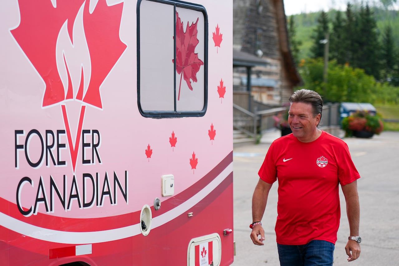 A man wearing a red t-shirt walks next to a bus with "Forever Canadian" and red maple leaves on the side.