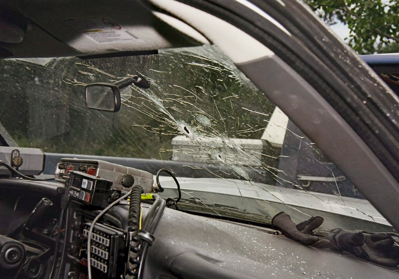 View from the inside of the dashboard and windshield of a police vehicle, with bullet holes and cracked glass.