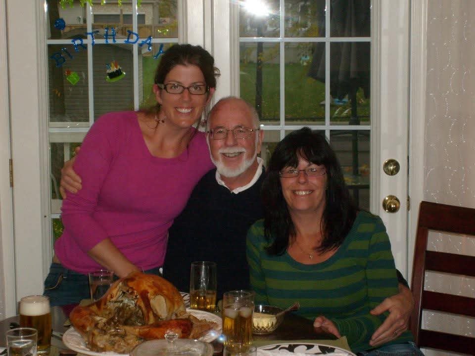 Two women stand beside their father at a dinner table.