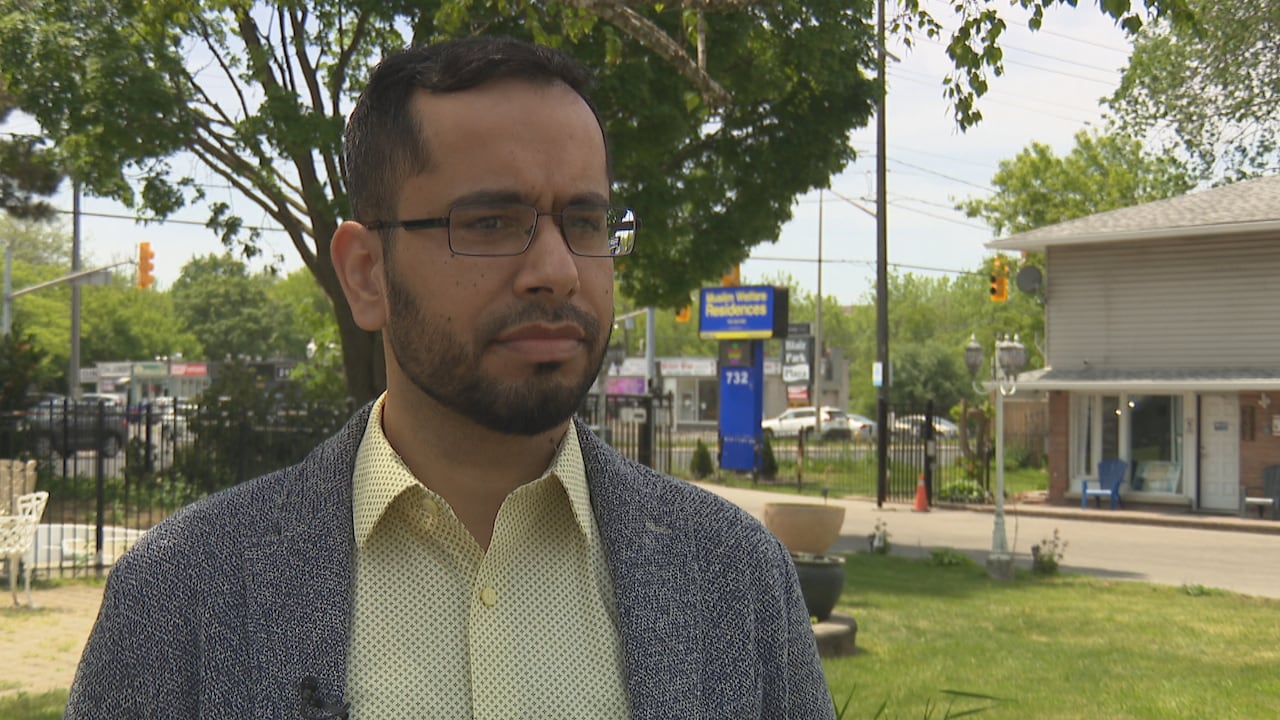 Man in jacket and wearing glasses speaks outside women's shelter.