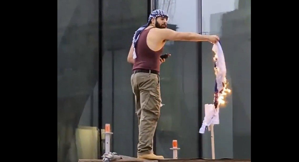 An anti-Israel activist sprays lighter fluid on a burning Israeli flag atop wooden scaffolding during a march in downtown Toronto on Friday, April 4 2025. Qabil Ibrahim, 26, of Toronto faces arson charges