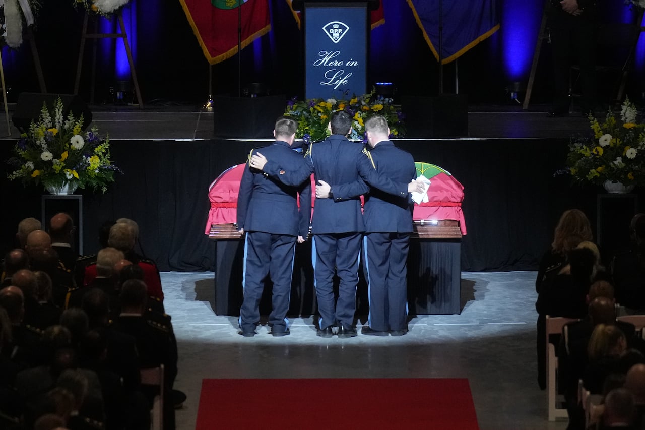 Three officers stand arm in arm in front of a casket