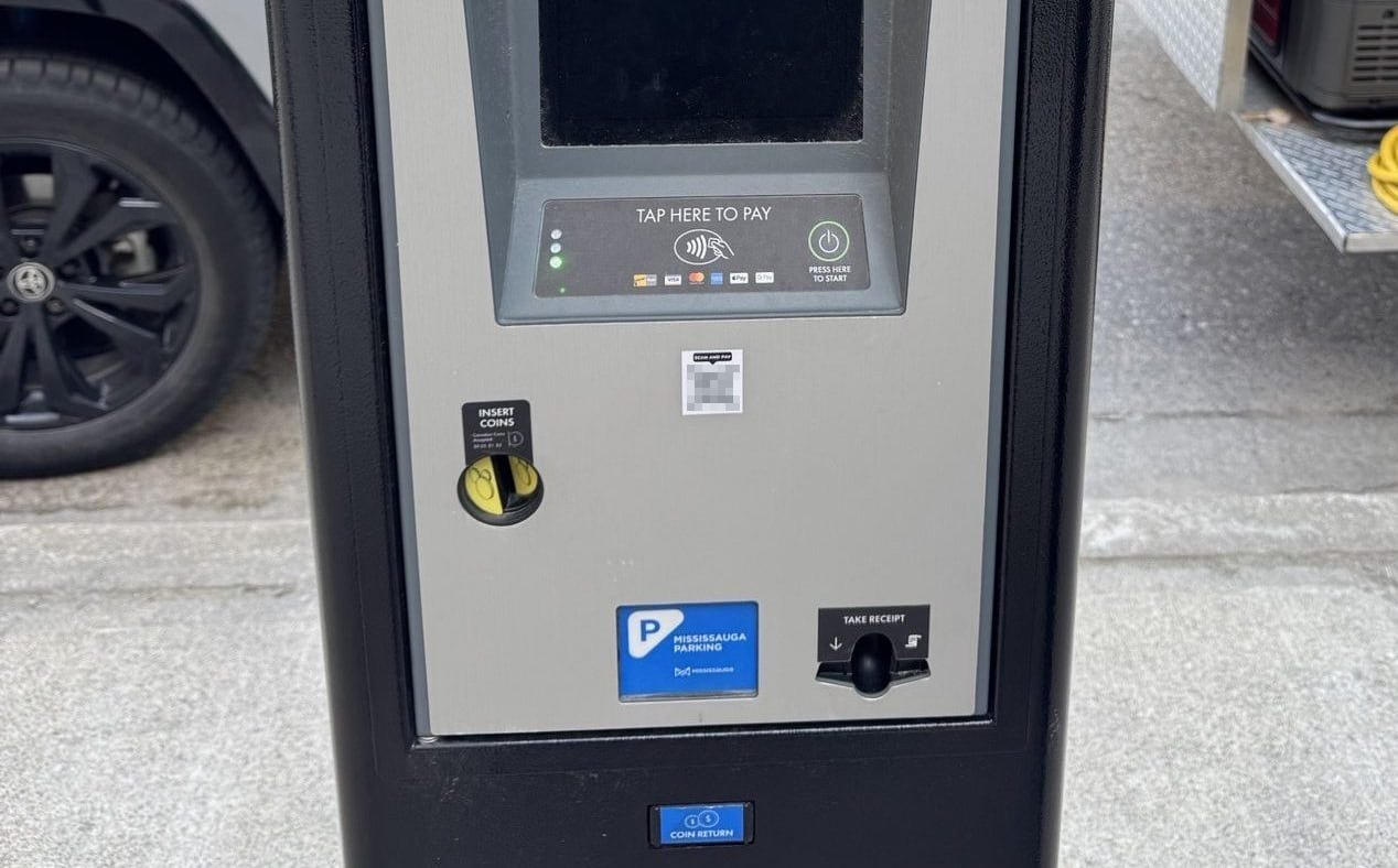 Black and grey parking machine with a blank, black screen, pad to tap your payment card and a small QR code that is blurred.