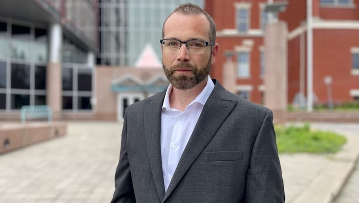 A man wearing glasses stands in front of a building.