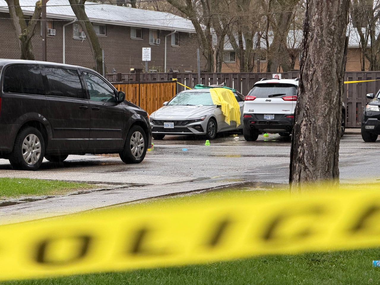 Car covered in tarp and police markers behind police tape.