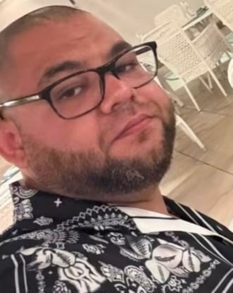Bearded man in button-up, short-sleeved black and white top wearing glasses
