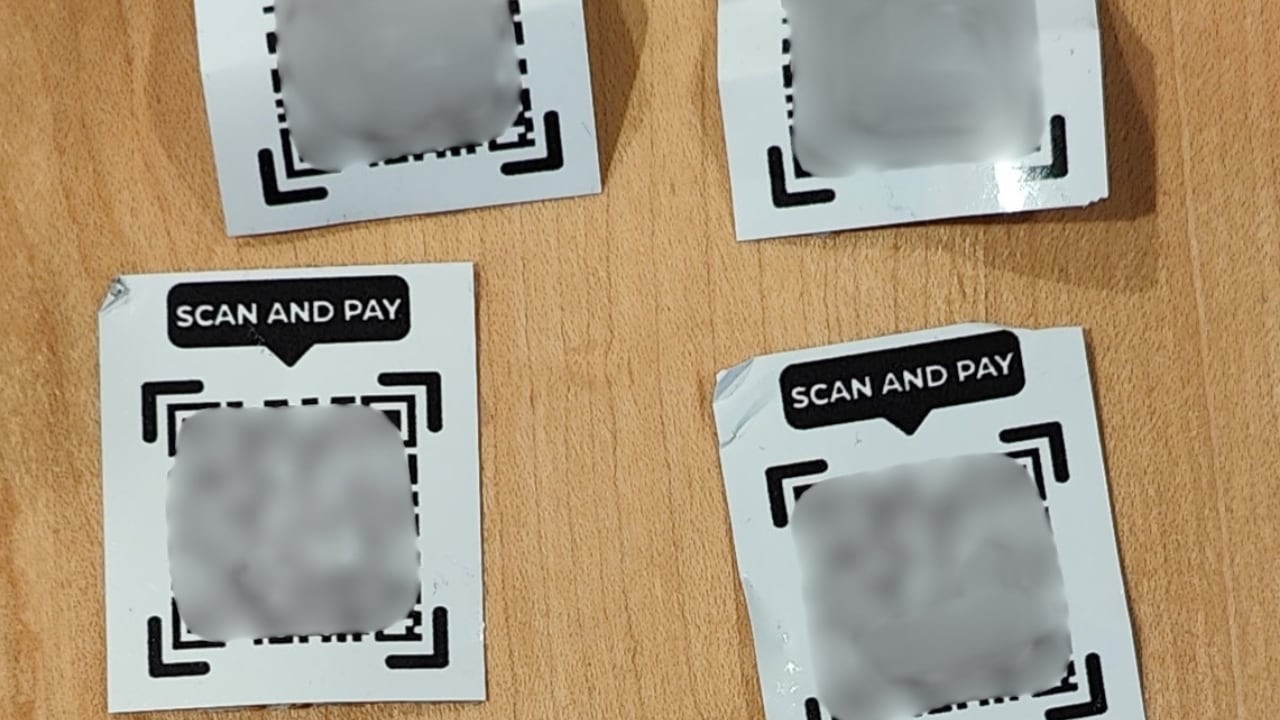 Four black and white QR codes sit on a table, blurred out because they lead to a scam website.