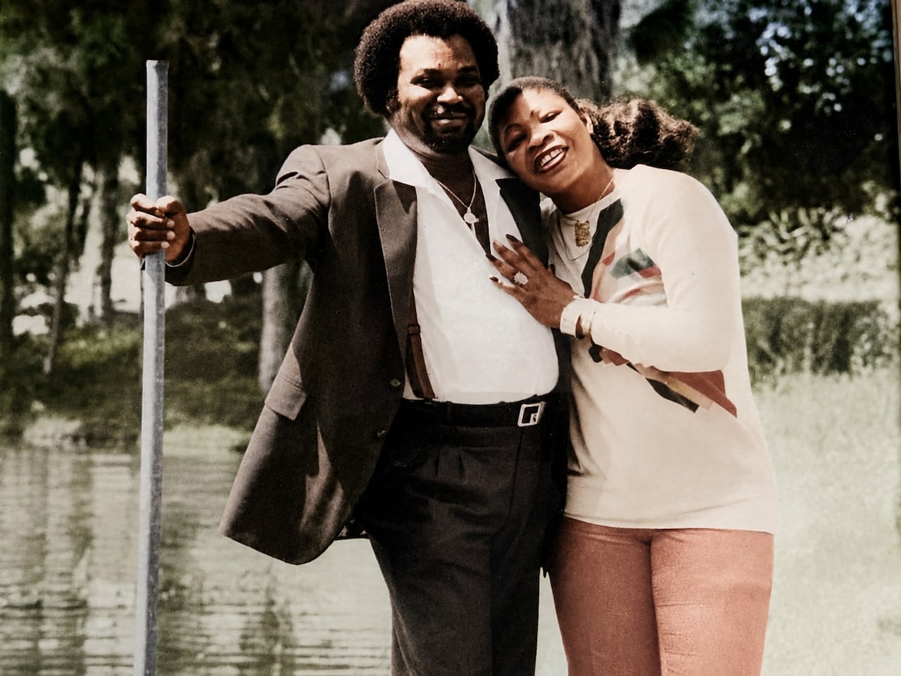 A couple stands for a photo in front of the camera, with a woman leaning on a man, smiling.