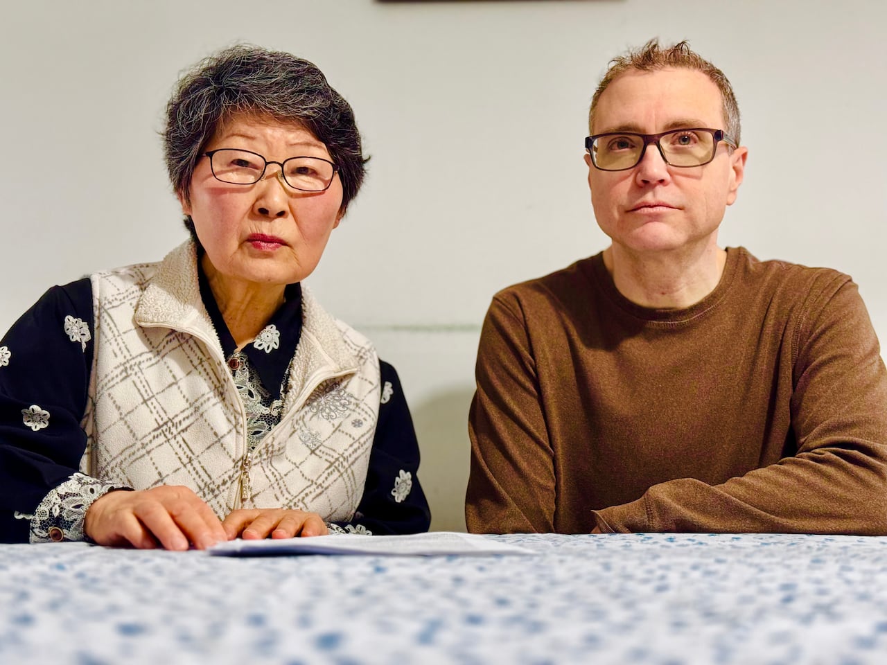 An elderly woman and younger man sit at a table with papers in front of them.