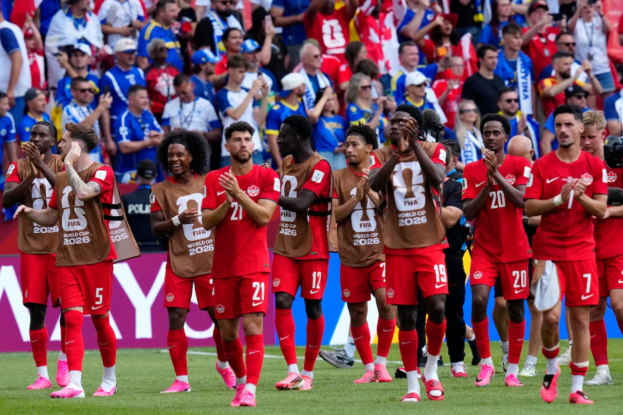 Team Canada players walk on the pitch, clapping and wearing their red uniforms.