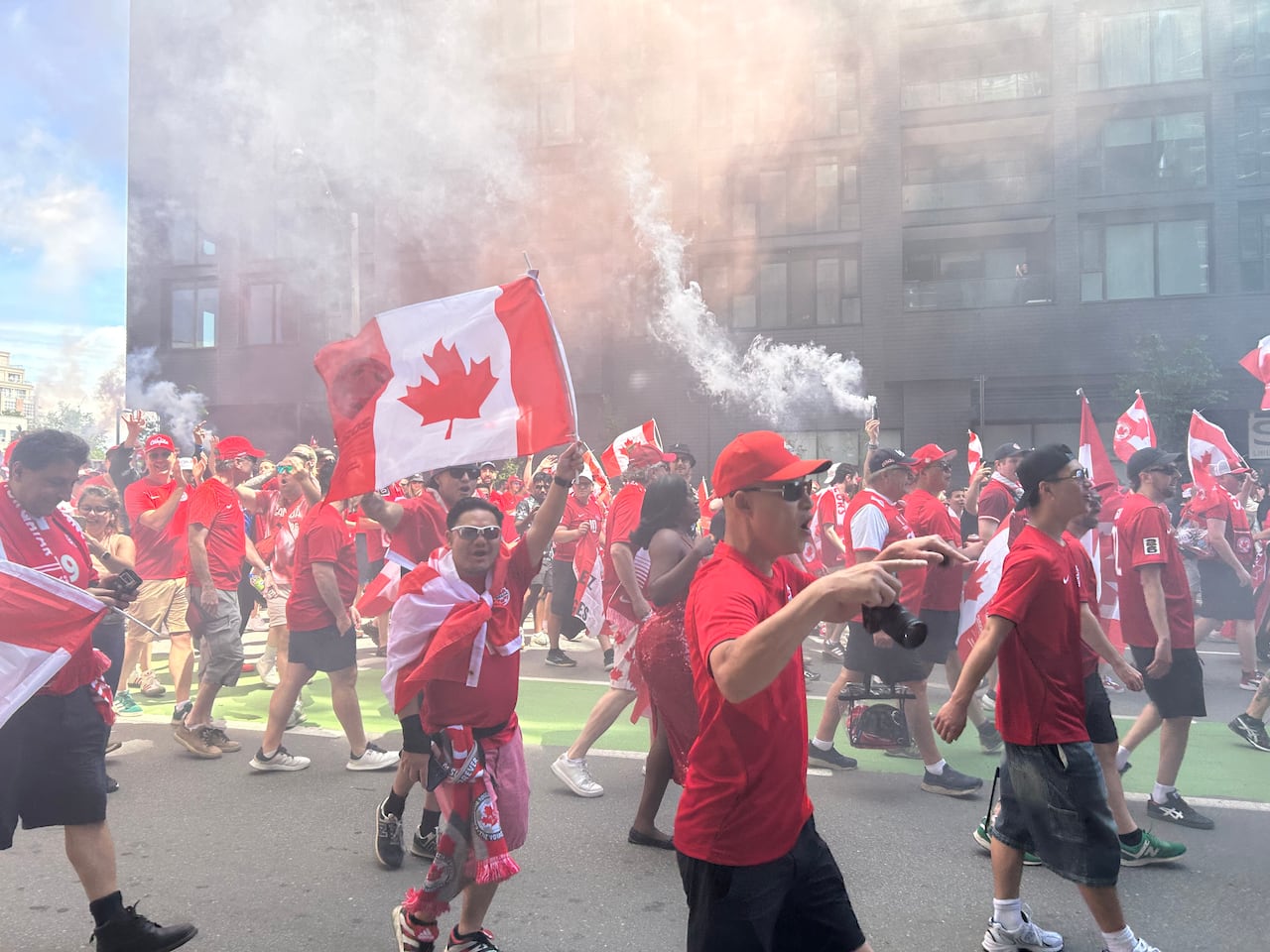 Fans march in red with Canadian flags with smoke bombs filling the air