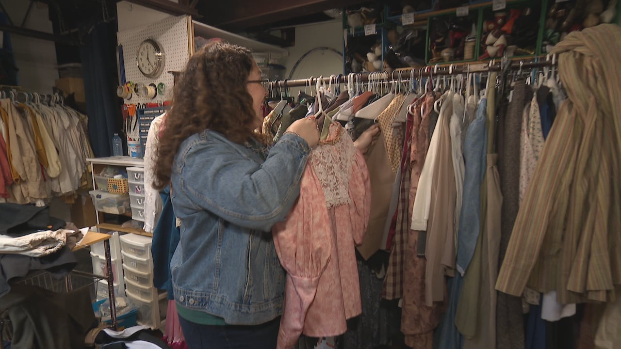 A woman pulling costumes out of a theatre stockroom