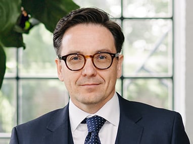 Headshot of Darcy Romaine, wearing a suit and glasses.