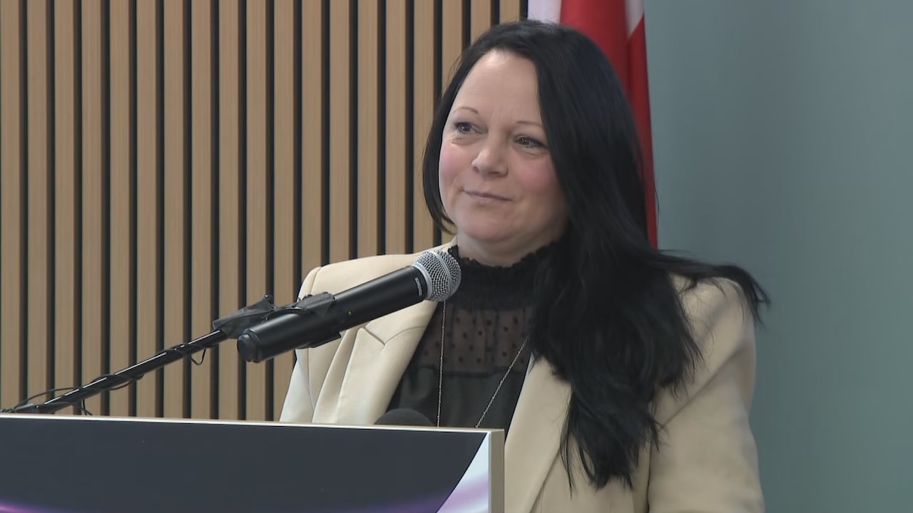 Woman in blazer standing behind podium smiling off-camera