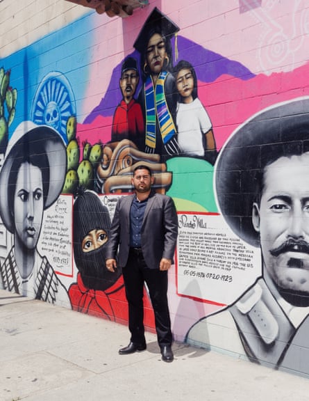 A man in a suit stands for a portrait in front of a colorful mural