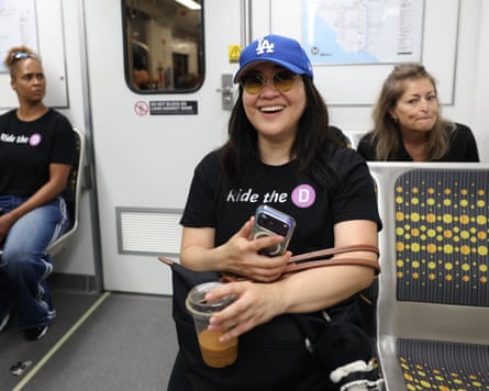 Smiling woman wearing “Ride the D” T-shirt and LA Dodgers hat on subway seat.