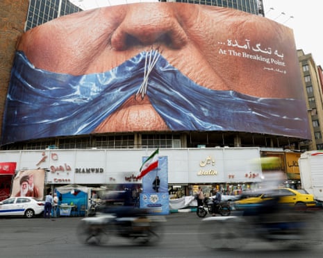 A large billboard shows a close-up face with a blue cloth covering the mouth, above busy street traffic in Tehran
